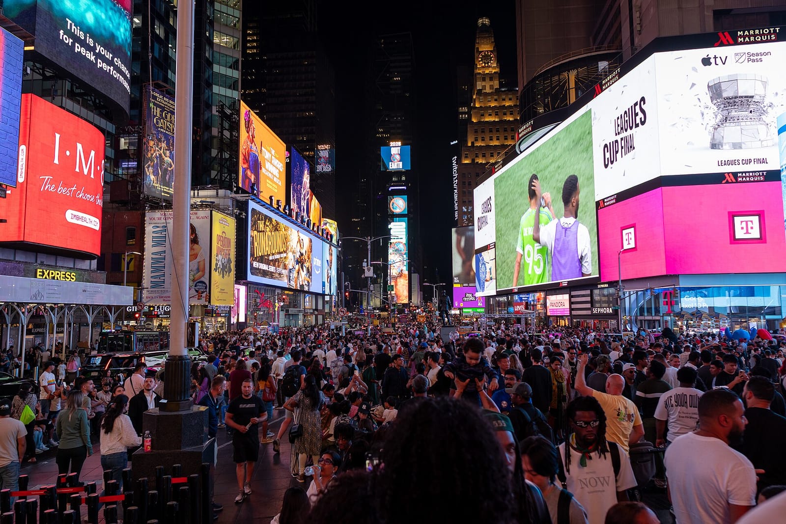 Crowds under illuminated advertising billboards in Times Square, New York, at night