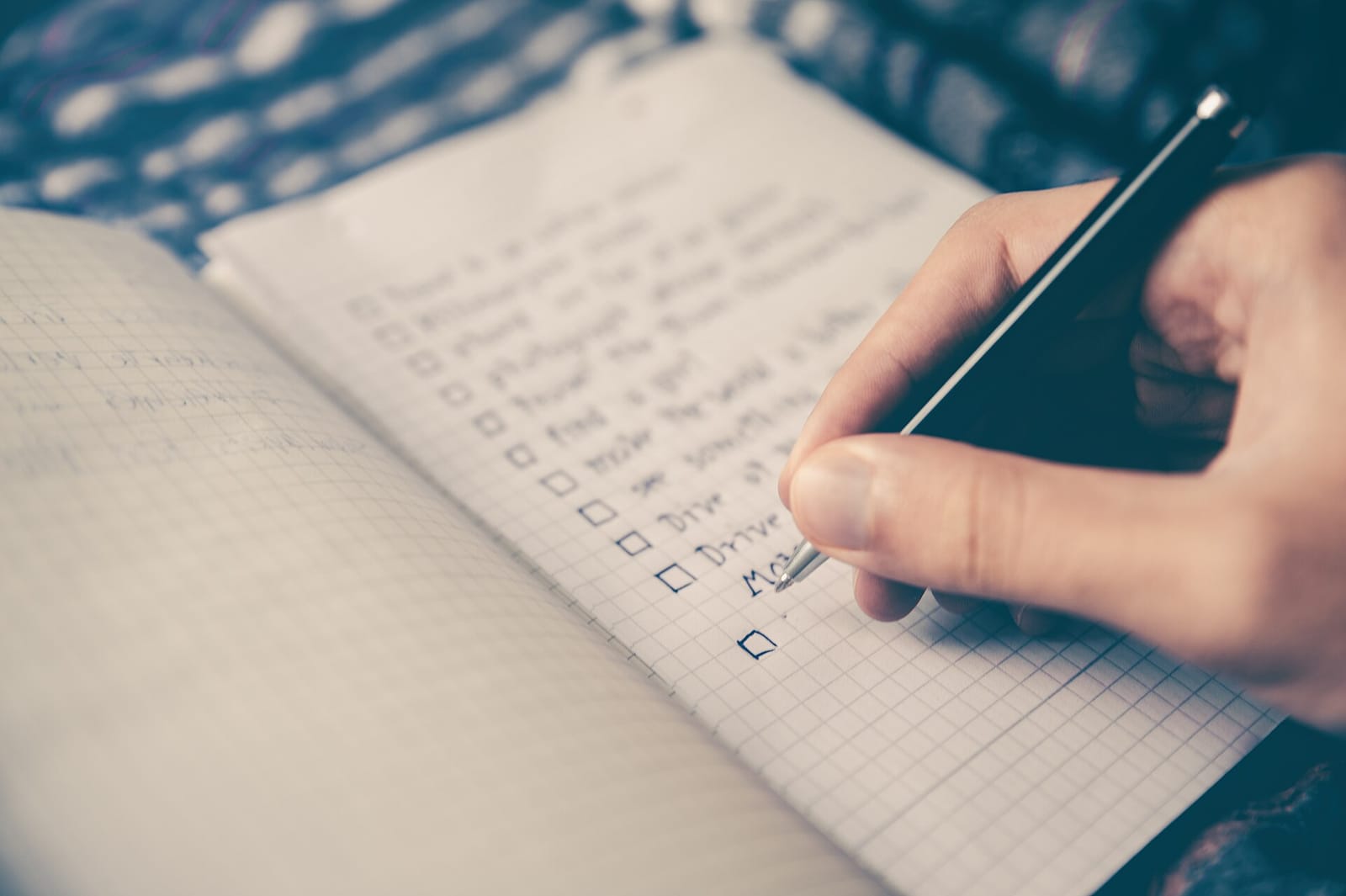 A hand writing a checklist with tick boxes in a notebook