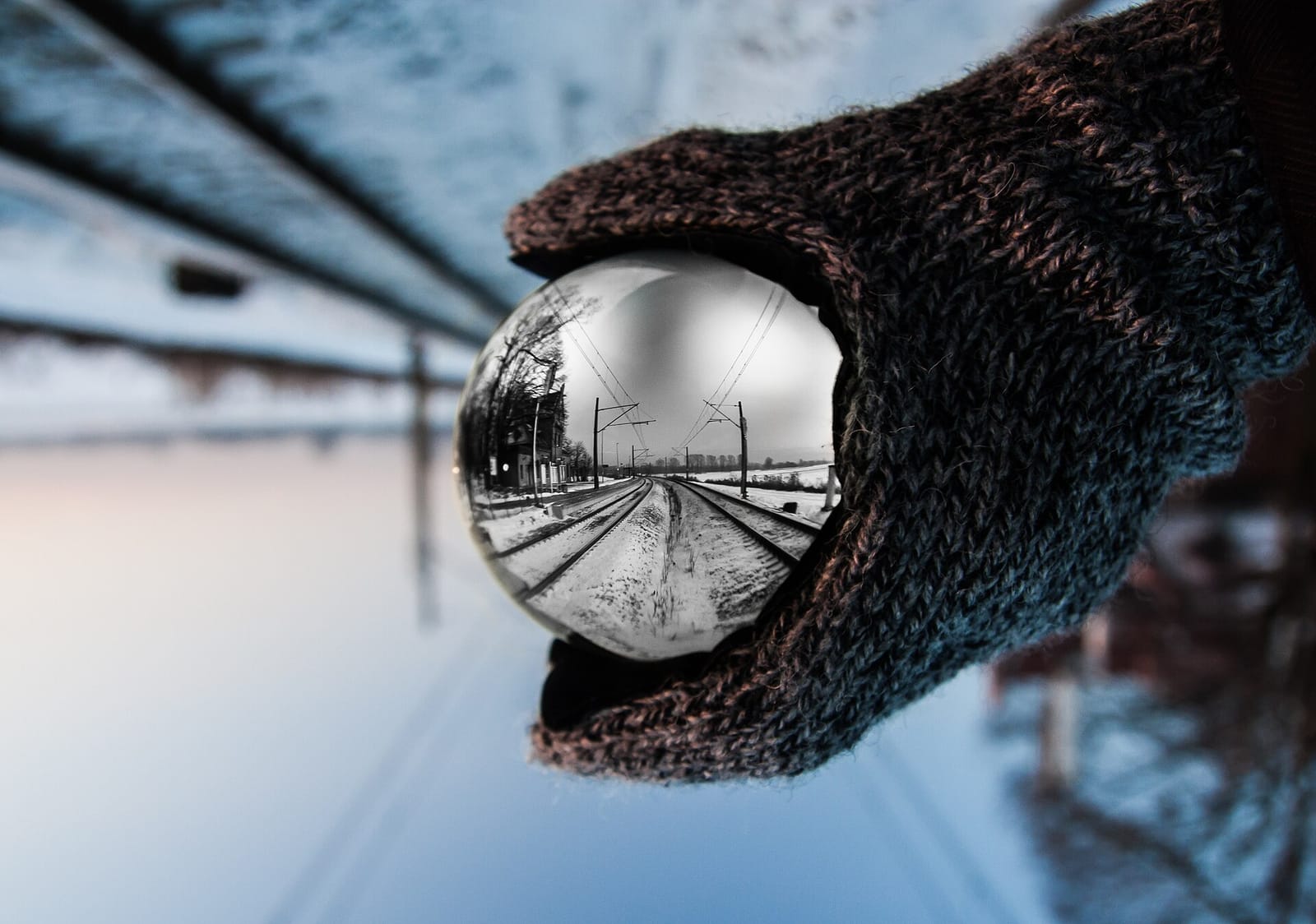 A gloved hand holding a glass ball that shows an upside-down view of a railway platform