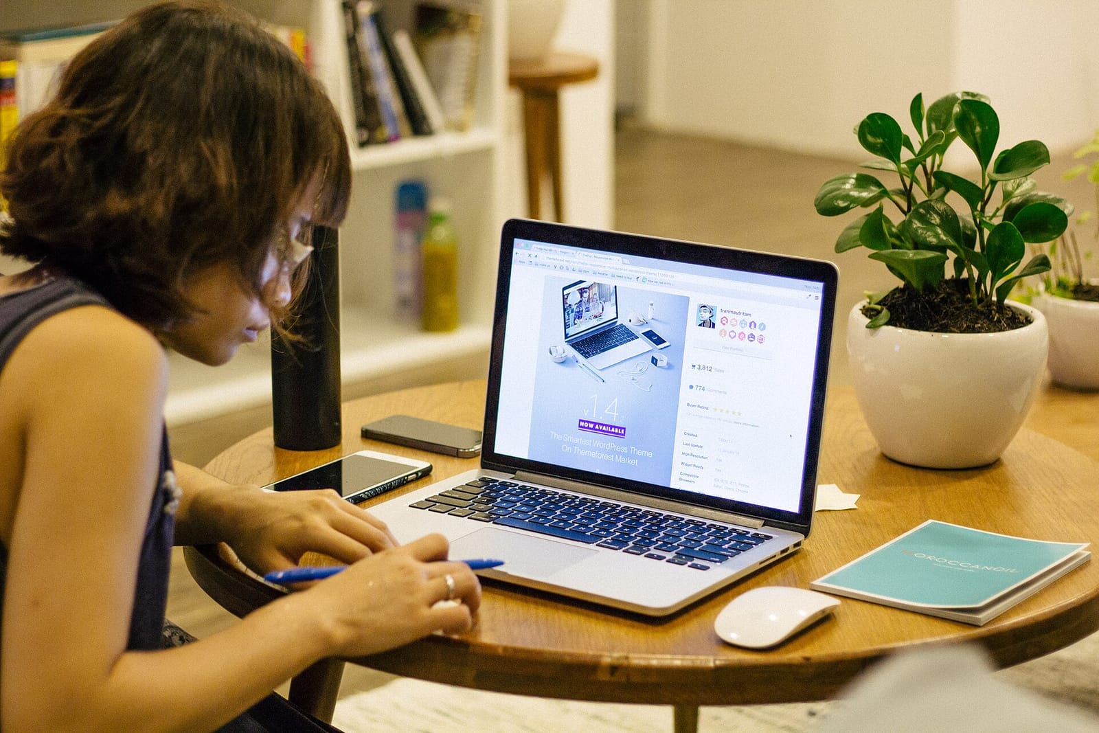 A woman taking handwritten notes while working on a laptop