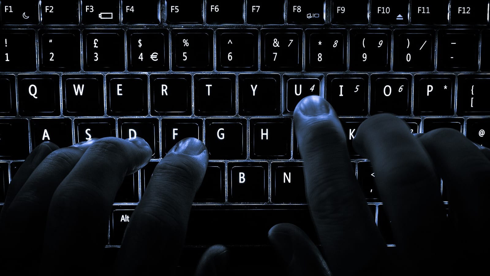 Hands typing on a backlit keyboard in the dark