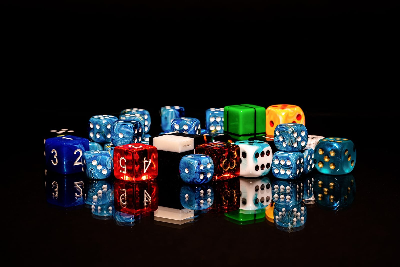 A pile of colourful six-sided dice on a black reflective surface