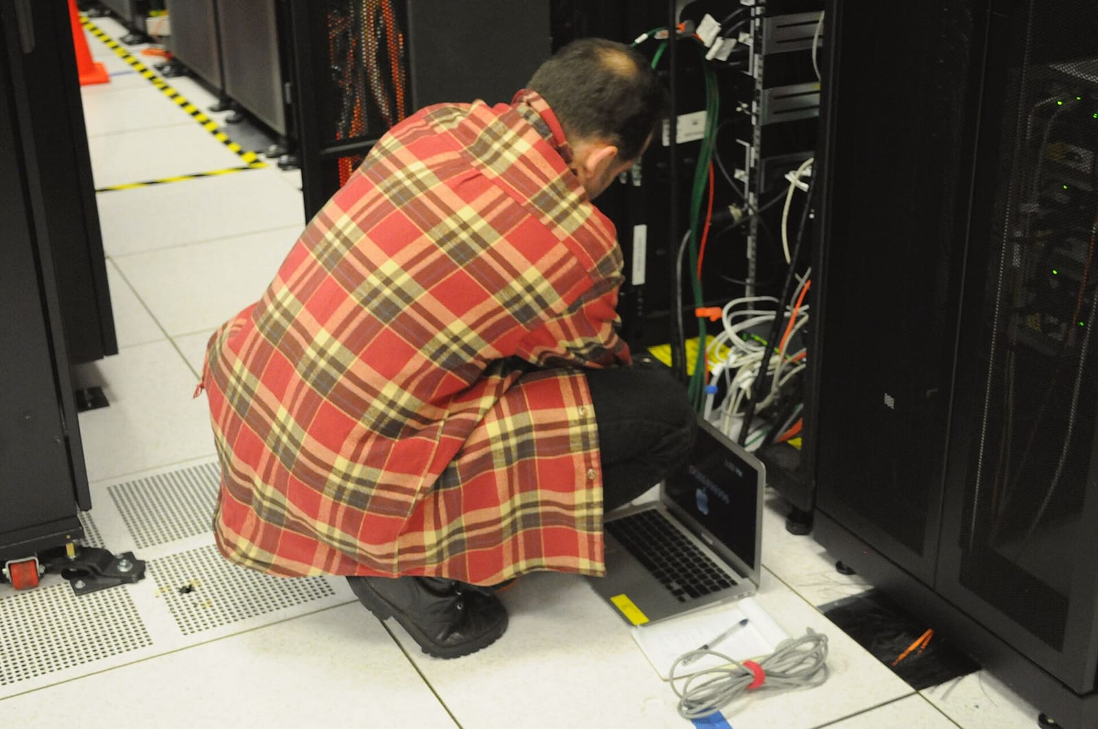 Technician with a laptop working at an open server rack in the NERSC data center