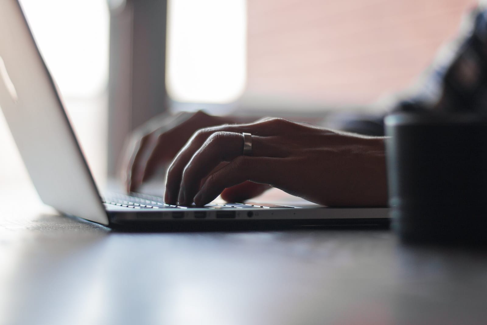 Hands typing on a laptop keyboard next to a mug