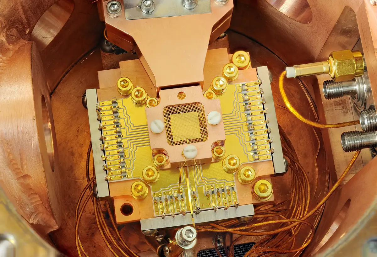 A gold-coloured ion-trap chip mounted on a circuit board inside a copper vacuum housing, surrounded by wires