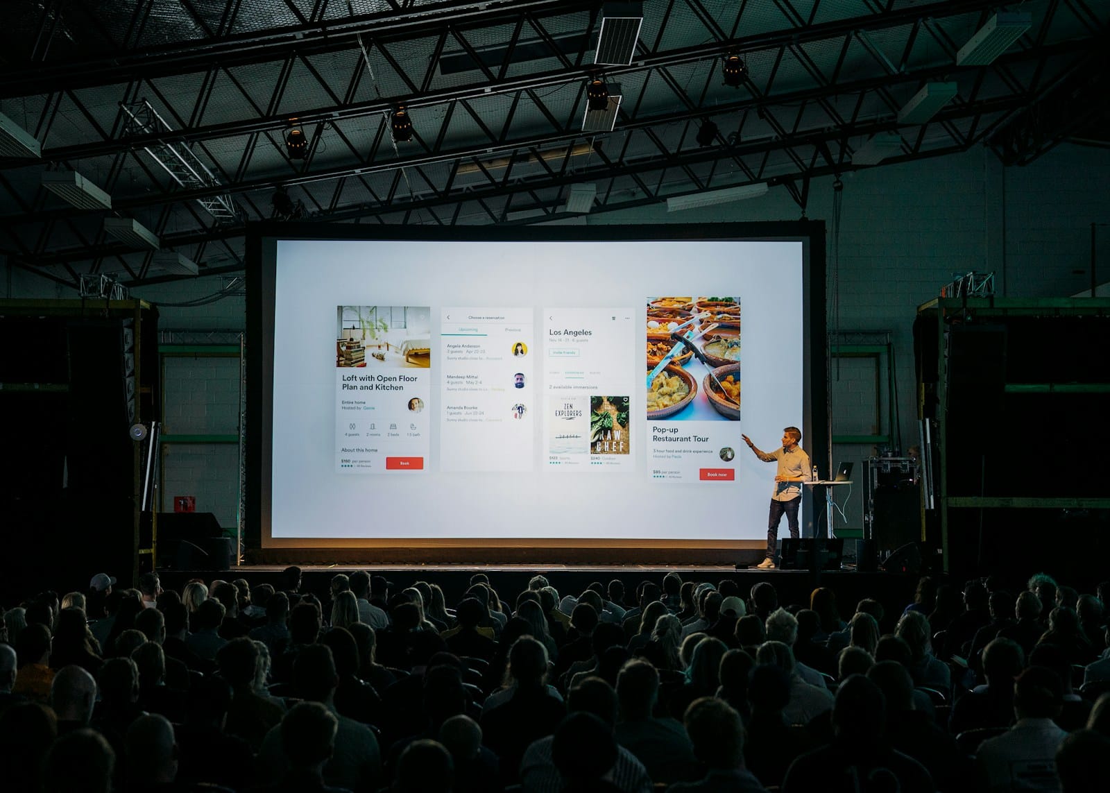 Speaker presenting in front of a large screen to an audience in a dim room