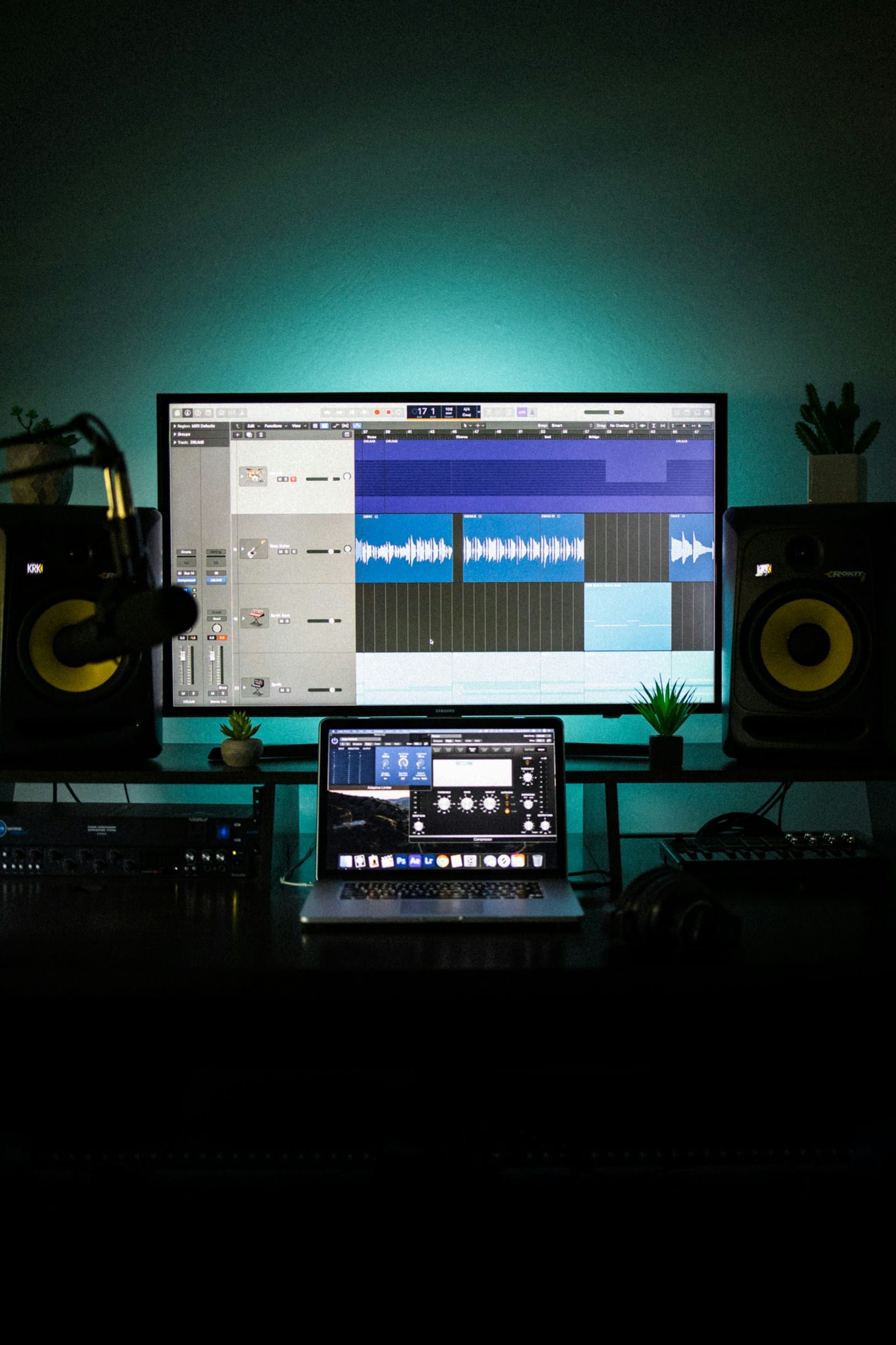 Computer monitor and laptop showing music production software in a dark workspace